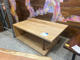 Angled view of a solid ash waterfall coffee table with an open-end design on a showroom floor.
