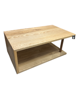 Angled view of a solid ash waterfall coffee table with an open-end design on a showroom floor.